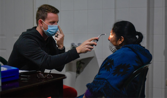 Optometrist examining a patient's eye with a handheld device.